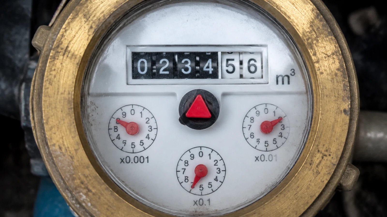 機械式水錶錶面近拍，中央紅色小三角形漏水指示器與黑底白字度數滾輪