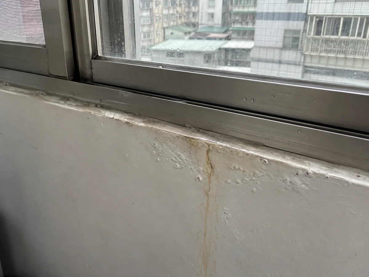 室內窗框下緣牆面油漆起泡、有黃色水痕，旁邊是鋁窗
